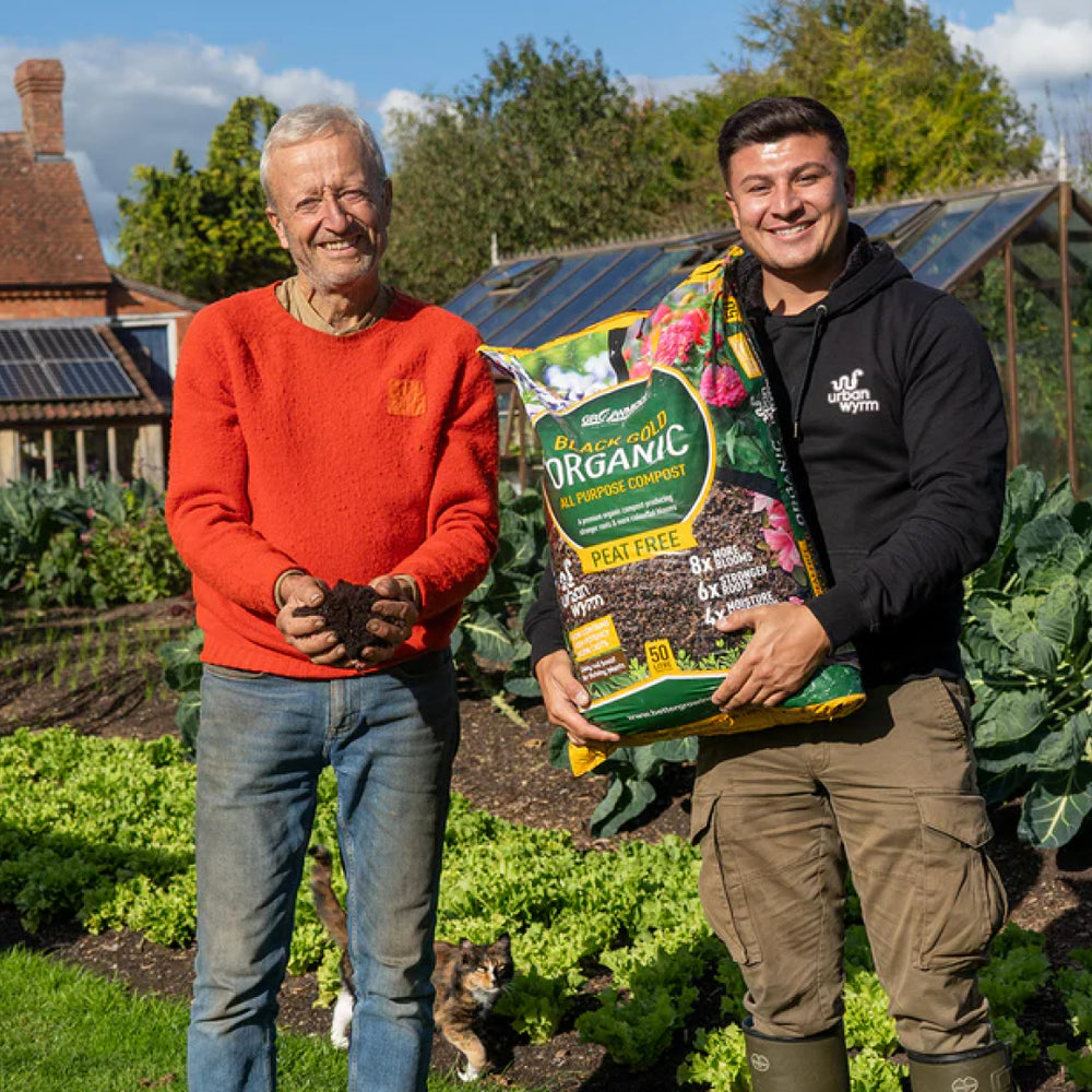 Charles Dowding and Ashley Day pose in a garden, with Ashley holding a bag of Growmoor Organic Black Gold compost